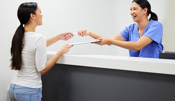 Smiling dental assistant handing patient form