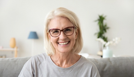 Older woman smiling on couch wearing glasses