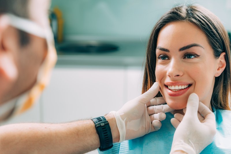 Dentist wearing mask putting gloved hands up to a woman's smile