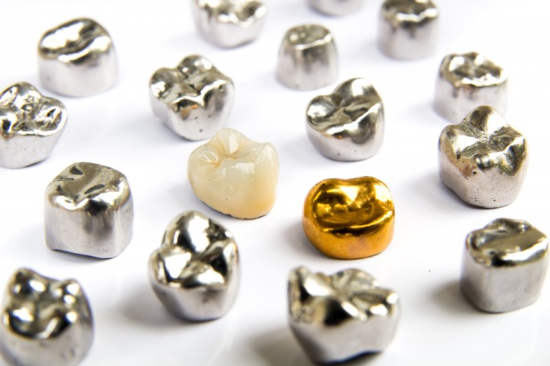 Various metal dental crowns of different shapes and sizes, mostly silver, one gold, and one tooth-colored non-metal one